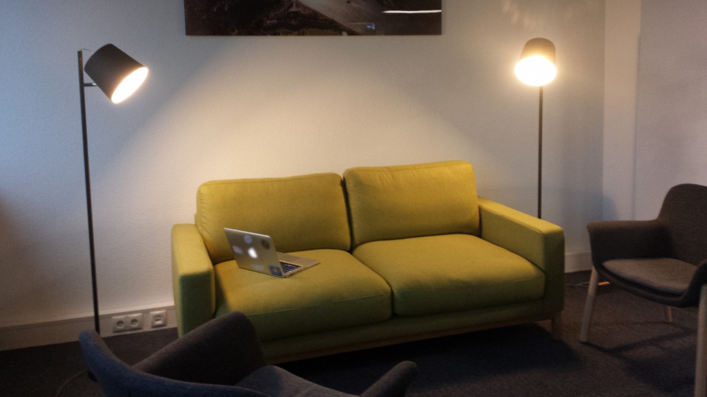 Grünes Sofa im Coworking Space. Links und rechts davon zwei Stehleuchten und zwei Sessel.